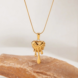 Pendentif cœur de lave doré poli sur fine chaîne serpent posé sur une pierre naturelle