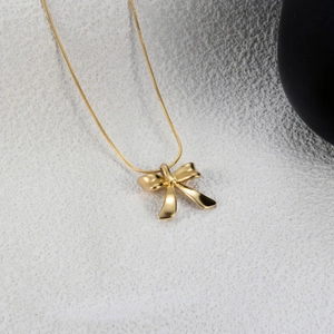 Elegant gold bow necklace with polished snake chain on white minimalist background