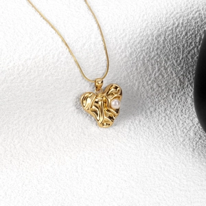 Golden irregular heart pendant necklace with pearl detail on a textured white surface