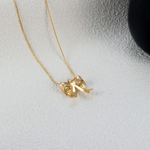 Detailed view of a gold bow pendant on a delicate snake chain over a white surface