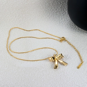 Detailed close-up of a polished gold bow pendant necklace with an adjustable steel chain