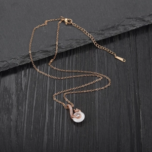 Detail of rose gold musical note necklace with white gemstone and pave crystals on a dark base