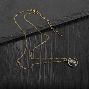 Macro view of gold chain with oval pendant featuring a black base and clear stone inlay