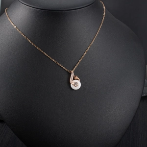 Detailed close-up of rose gold snail pendant necklace on a black mannequin display