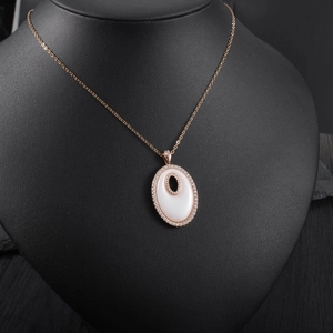 Gros plan du pendentif ovale en or rose avec incrustation blanche et cristaux sur buste noir