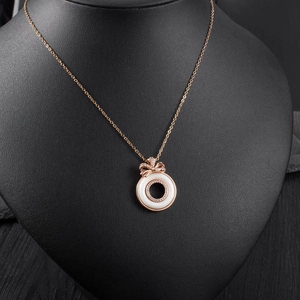 Detail of rose gold necklace with white ceramic ring and diamond bow pendant on model