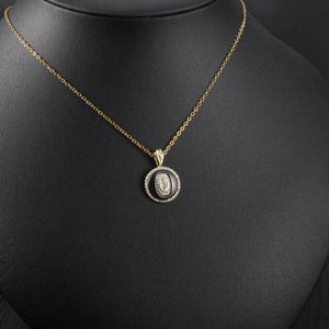 Detailed close-up of a luxury gold circular pendant with black enamel and zircons