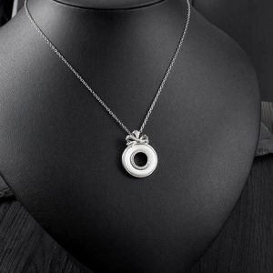 Detail of silver bow necklace with white ceramic ring and inlaid micro diamonds
