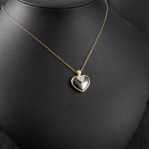 Détail d'un pendentif cœur noir avec cadre doré et breloque cœur sertie de diamants