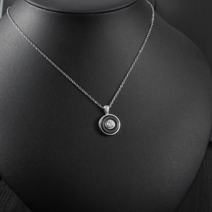 Detail of round pendant necklace with black enamel and diamonds on a black display bust