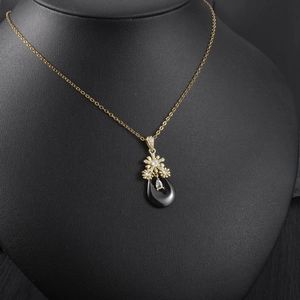 Détail du collier doré avec pendentif goutte noire et fleurs en cristal blanc