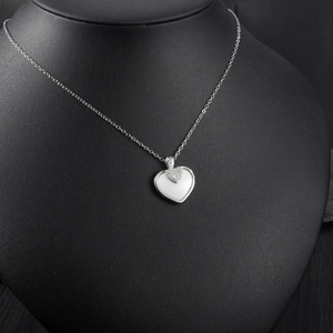 Gros plan d'un pendentif cœur en argent avec incrustation de nacre et pavé de diamants