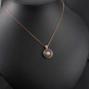 Detail of rose gold necklace with circular black inlay and sparkling diamond pendant