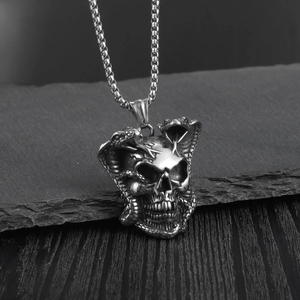 Macro shot of silver cobra wrapping around a skull pendant on a textured rock surface