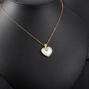 Détail du pendentif cœur doré avec émail blanc et cristaux sur un présentoir noir élégant