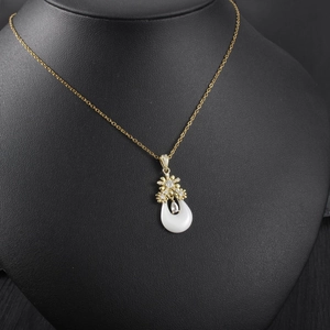 Vue détaillée d'un collier floral doré avec une pierre goutte blanche sur un buste noir