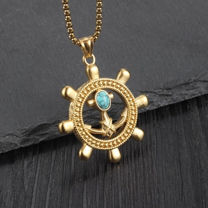 Goldene Halskette mit Anker und Steuerrad Anhänger sowie Türkisstein auf Steinuntergrund
