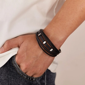 Detail of multi-layer black braided leather bracelet with silver metal charms on wrist