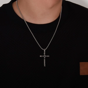 Detailed close-up of a vintage steel cross pendant with black stone on a male model