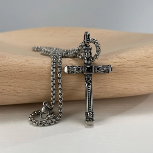 Macro view of gothic cross pendant with black gemstone and skull engraving on box chain