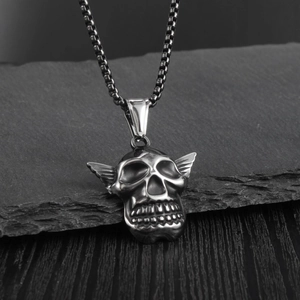 Close-up of vintage punk winged skull pendant on box chain over rustic stone background