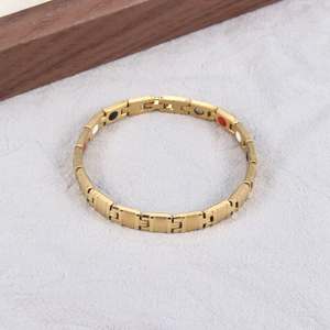 Detail of gold titanium magnetic therapy bracelet with inset health stones on white fabric