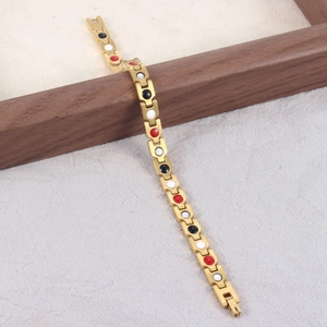 Bracciale magnetico dorato con pietre rosse, bianche e nere su sfondo di legno