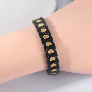 Detail of magnetic heart bracelet showing black link segments and gold embossed charms