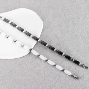 Dettaglio di braccialetti magnetici in ceramica bianchi e neri a forma di bambù su lino