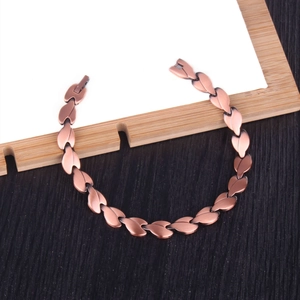 Vintage copper magnetic bracelet with leaf-shaped metal links on a dark wood background
