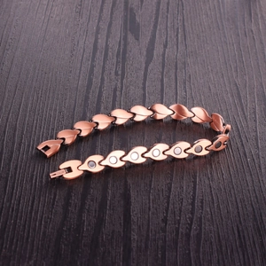 Close-up of leaf-shaped copper magnetic bracelet links with therapy magnets on wood
