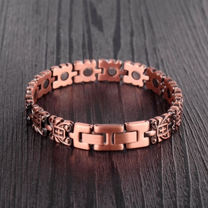 Detail of red copper magnetic therapy bracelet with vintage cross pattern on wood surface