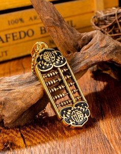Detailed shot of golden abacus pendant with Fu and Cai characters on a vintage wood background