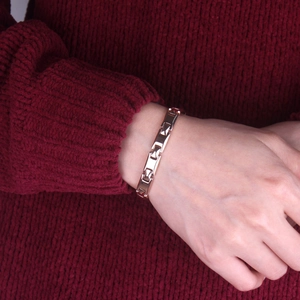 Close-up of a rose gold rectangle link bracelet worn on a wrist over a red sweater