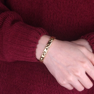 Detail of gold geometric link bracelet with triangle motifs worn over a red knit sweater