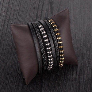Detail of multi-layer black leather bracelet with woven bands and metallic beads on a pillow