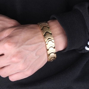 Close-up of wide gold magnetic energy bracelet featuring linked wave-shaped metal links
