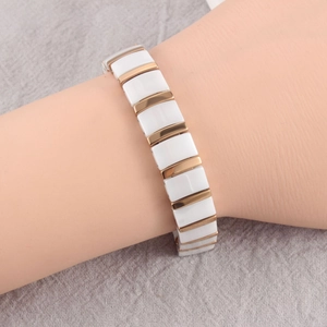 Detailed view of white ceramic and gold metal link bracelet on a textured grey background