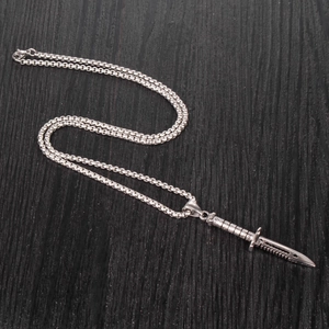 Gros plan du pendentif poignard argenté avec chaîne box sur bois sombre