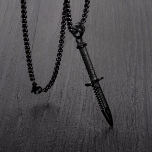 Détail d'un pendentif poignard noir avec lame dentelée et chaîne à billes
