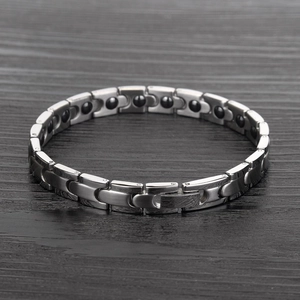 Macro detail of men's magnetic health bracelet with silver steel links on wood background