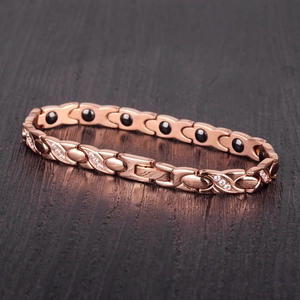 Detail of rose gold X-shape bracelet with zircons and magnetic therapy stones on wood