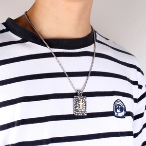 Détail du pendentif rectangulaire gaufré avec croix dorée sur une chaîne en argent