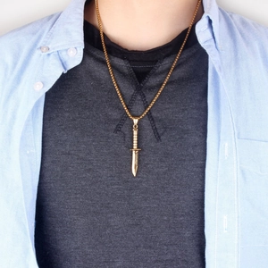 Gros plan d'un collier pendentif dague dorée avec poignée détaillée sur tenue homme