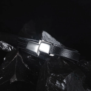 Detail of black woven leather bracelet with polished silver magnetic clasp on dark stones