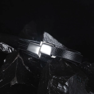 Close-up of men's black leather bracelet featuring a polished silver metal clasp on black rock