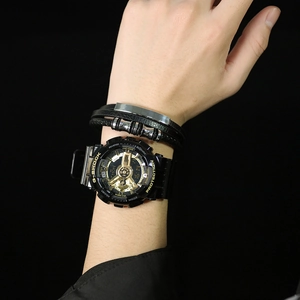 Close-up of a dual-display black and gold watch with a woven leather bracelet on wrist