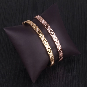 Detail of gold and rose gold X-shape bracelets with cubic zirconia on jewelry cushion