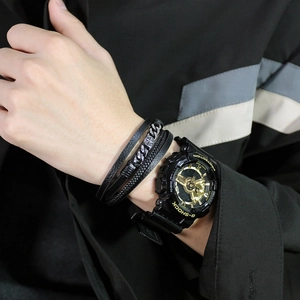 Detail of men's layered leather bracelet with compass charm and sporty watch on wrist