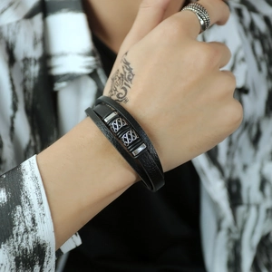 Detail of multi-layer black leather bracelet with engraved silver metal charms on wrist